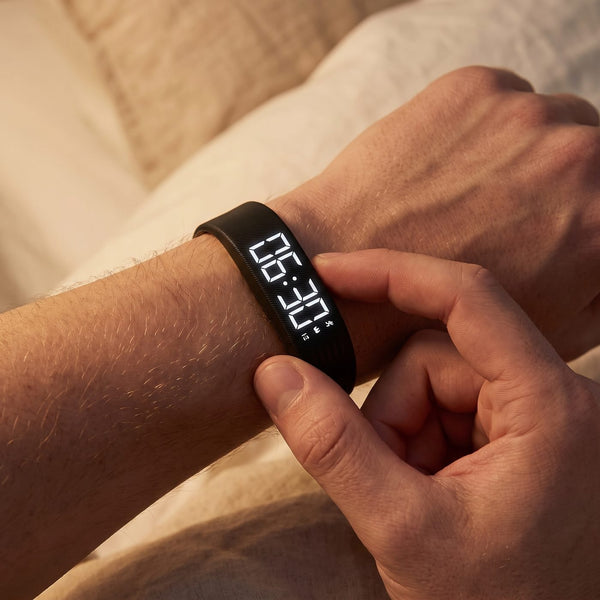 A finger presses the button of the black band, the display lit at 06:30.