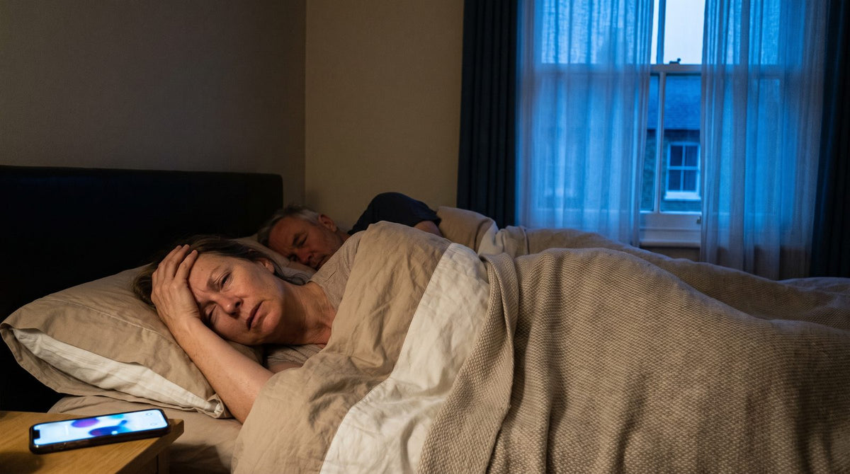 Before dawn, a woman is woken by her partner's phone alarm while he sleeps on.